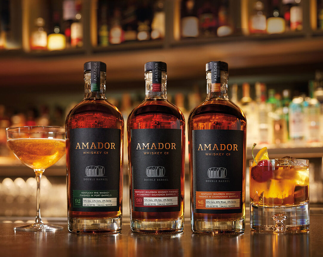 Color image of three bottles of Amador Whiskey Co whiskey with a glass of whiskey on a bar