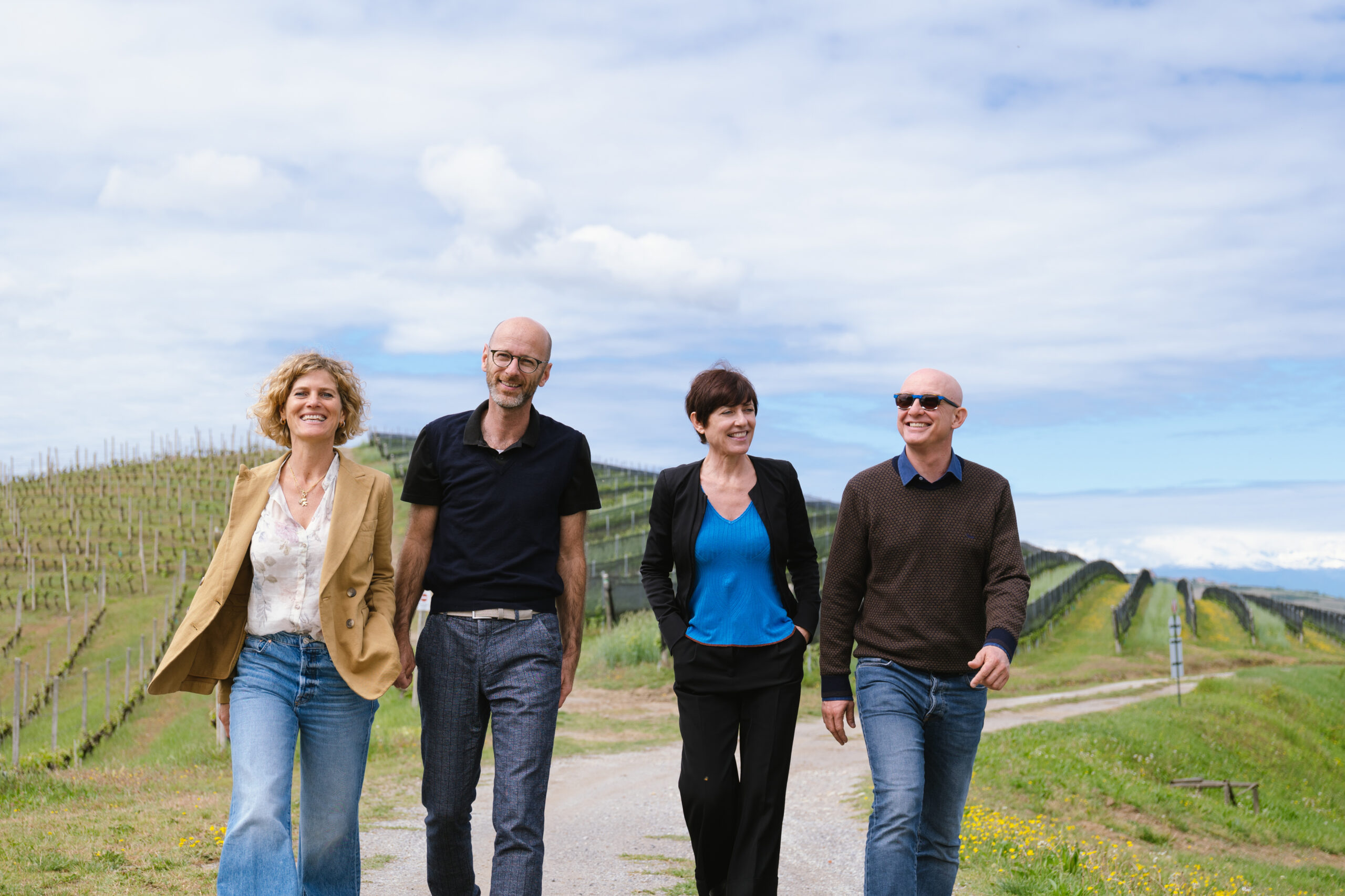 Color image of 4 members of the Ceretto family walking among grapevines