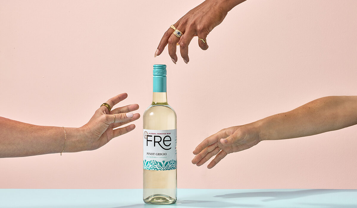 Color image of 3 hands reaching for a bottle of FRE alcohol removed Pinot Grigio